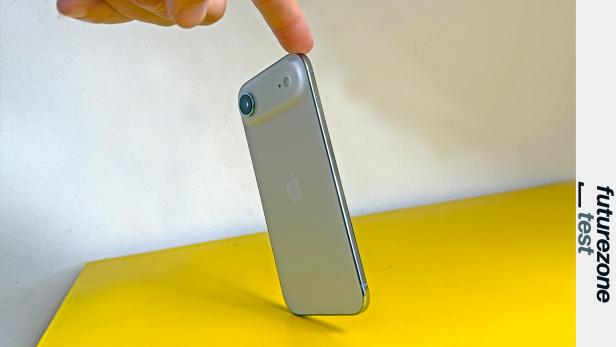 Ein Finger berührt ein silbernes iPhone auf einem gelben Tisch.