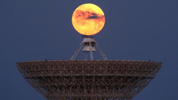 Eine grosse Satellitenschüssel steht im Vordergrund, darüber scheint der orange Vollmond exakt auf ihrer Spitze zu ruhen.