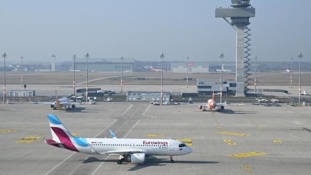 Ein Flugzeug von Eurowings rollt auf dem Vorfeld eines Flughafens, im Hintergrund steht ein hoher Kontrollturm.
