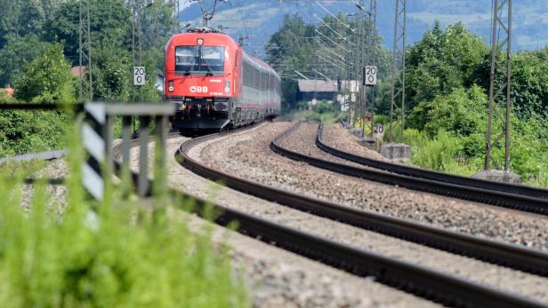 Ein roter Zug der ÖBB fährt auf einer kurvigen Bahnstrecke durch eine grüne, ländliche Landschaft.