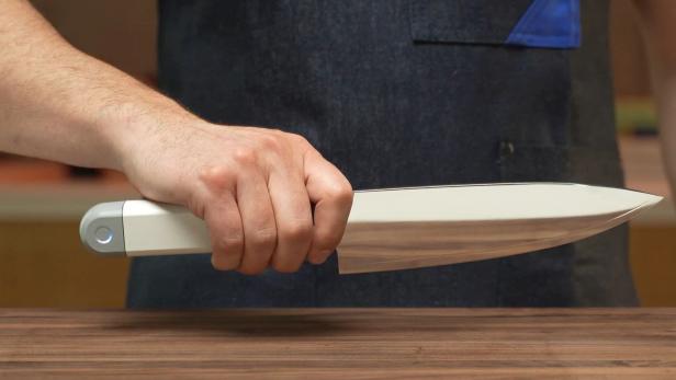 Eine Hand hält das Messer über einer hölzernen Arbeitsplatte.