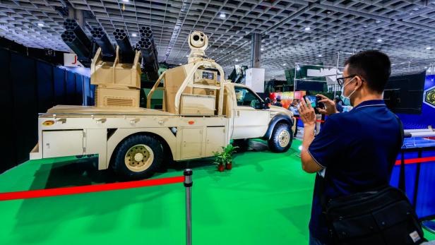 Ein Mann fotografiert ein militärisches Fahrzeug mit Raketenwerfern und Überwachungstechnik auf einer Messe.
