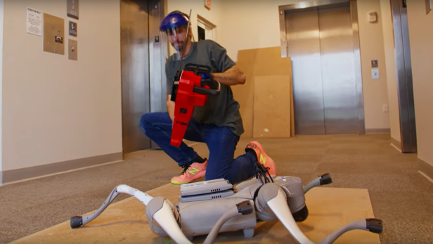 Ein Mann hält eine Kettensäge in der Hand bevor er die Beine eines Roboters absägt