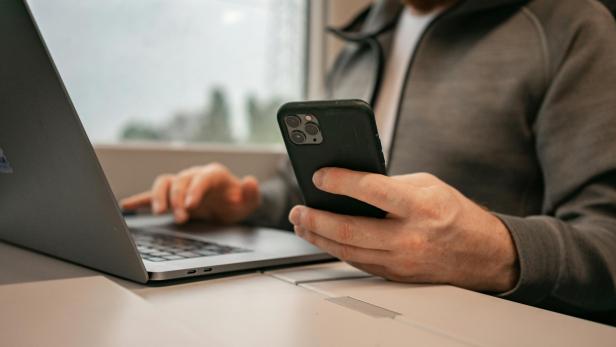 Person sitzt mit Laptop und Smartphone an einem Tisch
