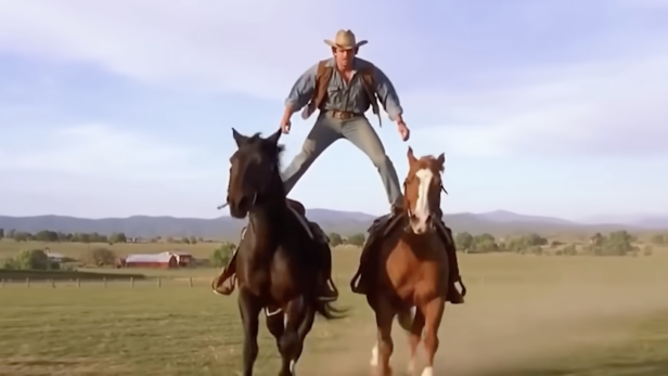 ein Mann der auf 2 Pferden steht und reitet 