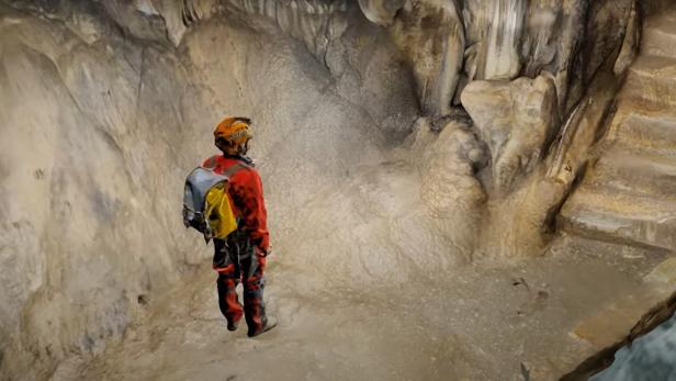 Screenshot des 3D-Modell-Videos einer Höhle, darauf eine Person in rot-oranger Höhlenausrüstung