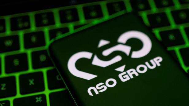 NSO Group Logo auf einem Smartphone, dass vor grün beleuchteter Computertastatur liegt