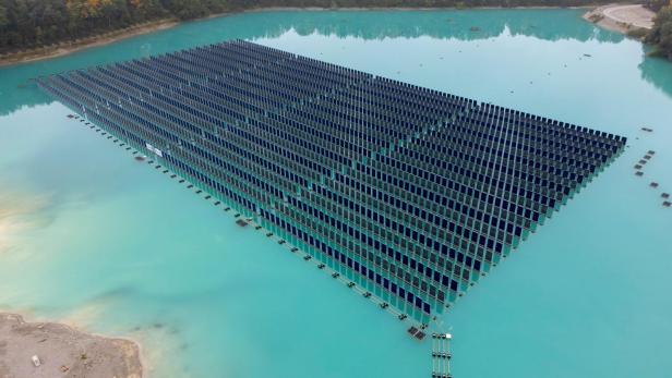 Eine große schwimmende Solaranlage befindet sich auf türkisfarbenem Wasser, umgeben von Bäumen und einer kleinen Landfläche.