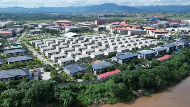Luftaufnahme einer Siedlung aus gleichförmigen grauen Häusern entlang eines braunen Flusses
