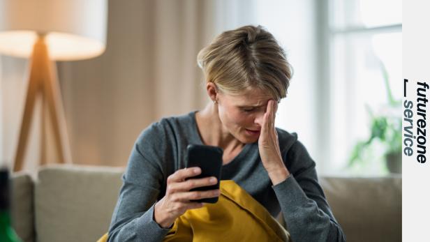 Eine verzweifelte Frau sitzt auf der Couch vor ihrem Smartphone