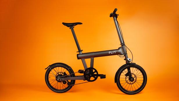 das Flit M2 Faltrad in grau und schwarz vor orangem Hintergrund