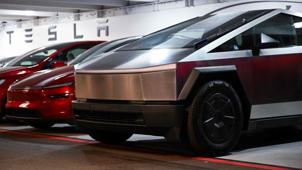 Ein Tesla Cybertruck steht neben einem roten Tesla in einer Garage unter dem Tesla-Schriftzug.