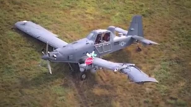 Beschädigtes Militärflugzeug mit abgebrochener Tragfläche und Stoppschild auf Wiese.