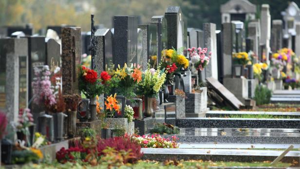 Reihe von Grabsteinen mit vielen bunten Blumensträußen und Pflanzen auf den Gräbern.