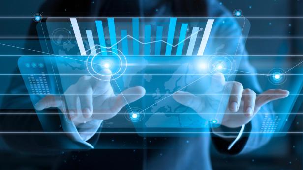 Person in Anzug tippt auf transparentes Display mit blauen Balkendiagrammen und Weltkarte im Hintergrund.
