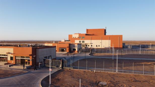 Das TMSR-Gebäude mit Zaun steht in einer weiten, offenen Landschaft unter blauem Himmel.