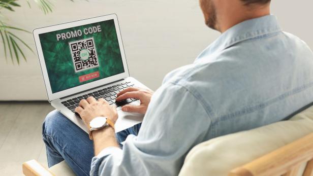 Mann arbeitet an Laptop, auf dessen Bildschirm ein QR-Code angezeigt wird.