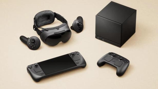 Auf beigem Grund liegen eine VR-Brille, zwei Controller, ein Steam Deck und eine schwarze Box.