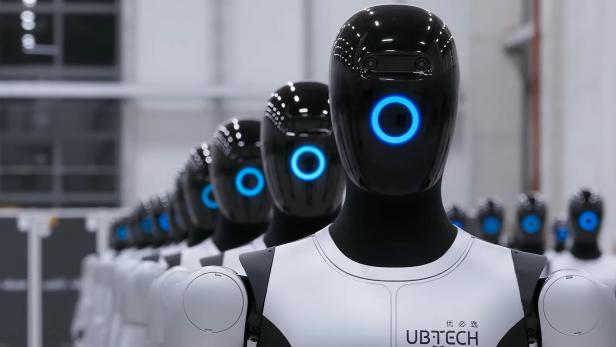 Mehrere Walker S2 Roboter von Ubtech Robotics stehen in einer Halle in Reih und Glied.