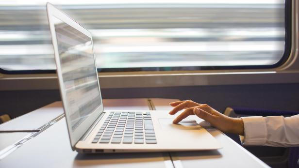 Eine Person arbeitet an einem Laptop auf einem Tisch in einem fahrenden Zug.