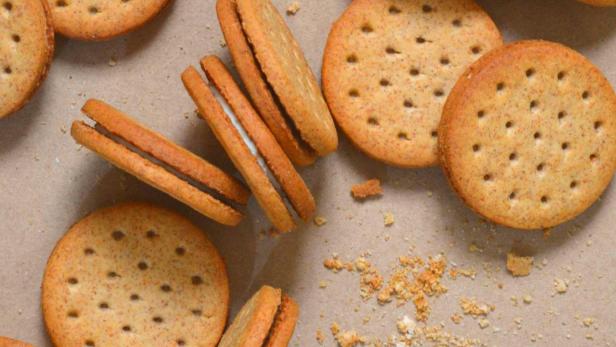 Mehrere Doppelkekse und Keksbrösel auf braunem Untergrund.