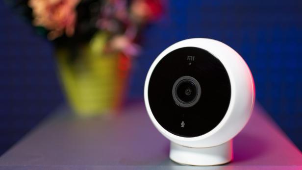 Weiße Überwachungskamera auf Tisch, im Hintergrund ein unscharfer Blumenstrauß.