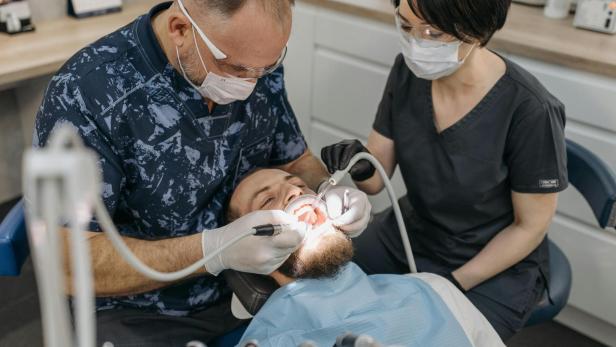 Zahnarzt behandelt einen Patienten, während eine Assistentin daneben sitzt und hilft.