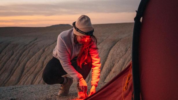 Eine Person mit Stirnlampe ZB7H von Zweibrüder befestigt bei Sonnenuntergang ein Nordisk-Zelt in felsiger Landschaft.