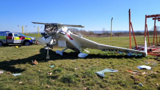 Ein beschädigtes Kleinflugzeug liegt auf einer Wiese neben Trümmern und einem Einsatzfahrzeug.