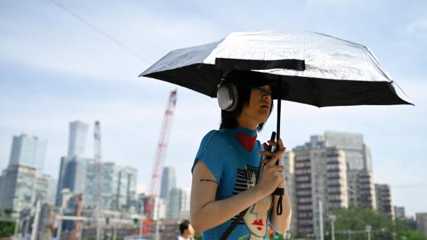 Eine Person mit Kopfhörern hält einen silbernen Regenschirm in einer städtischen Umgebung.
