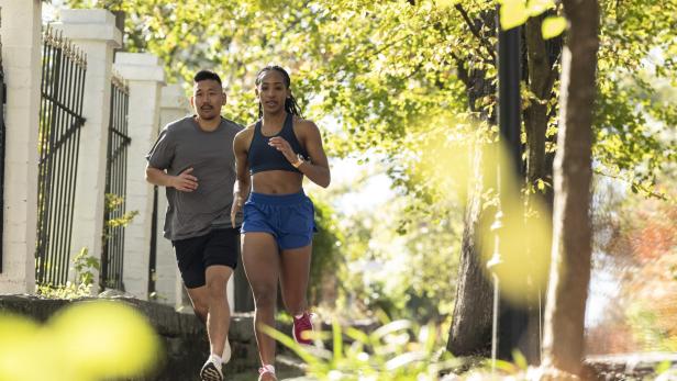 Zwei Personen joggen auf einem sonnigen Weg mit Bäumen.