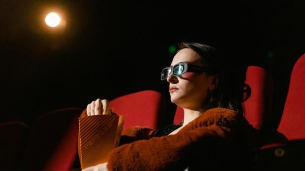 Frau mit 3D-Brille sitzt im Kinosessel und hält eine Popcorntüte.