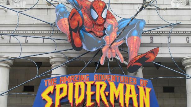 Eine große Spider-Man-Figur mit Spinnennetz und dem Schriftzug „The Amazing Adventures of Spider-Man“ vor einem Gebäude mit Uhr.