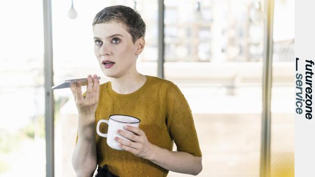 Eine Frau mit kurzem Haar telefoniert mit dem Handy und hält eine Tasse.