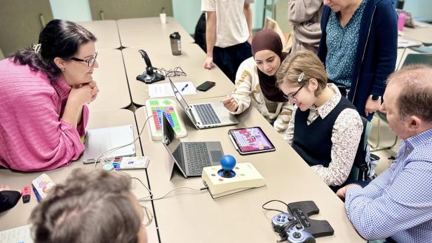 Mehrere Personen testen gemeinsam an einem Tisch technische Hilfsmittel und Tablets.