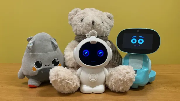 Vier verschiedene KI-Spielzeuge, darunter Plüschtiere und Roboter, auf einem Holztisch.