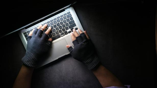 Person mit fingerlosen Handschuhen tippt auf einer Laptop-Tastatur im Dunkeln.