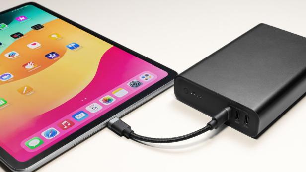 Ein Tablet wird über ein Kabel mit einer externen Powerbank verbunden und aufgeladen.