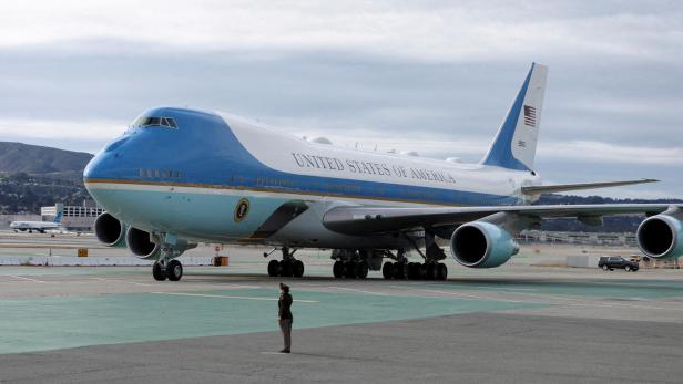 Großes blau-weißes Flugzeug mit der Aufschrift „United States of America“ steht auf dem Rollfeld, eine Person davor.