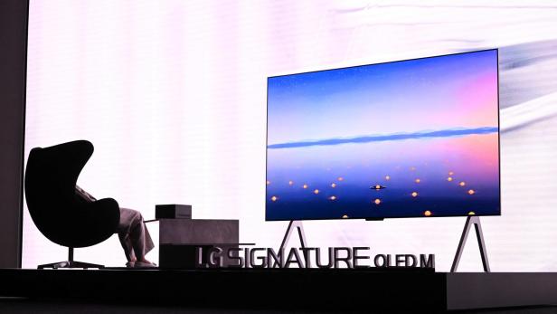 Eine Person sitzt in einem modernen Sessel vor einem großen Fernseher mit farbenfrohem Landschaftsbild.