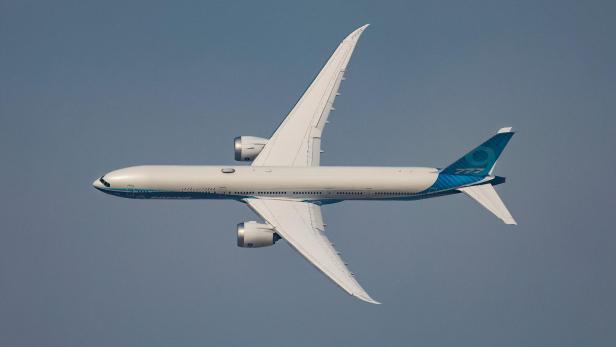 Ein weißes Boeing 777 Flugzeug fliegt am blauen Himmel.