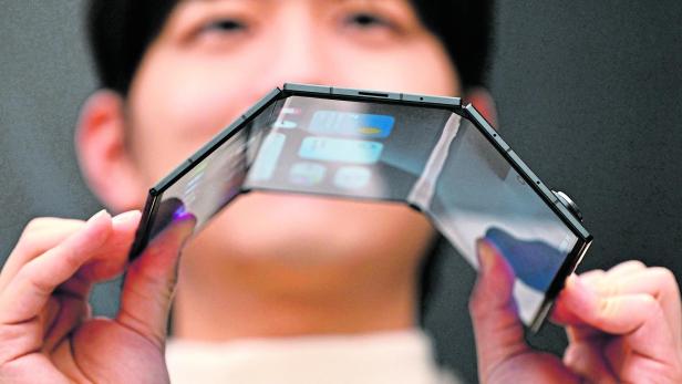 Eine Person hält ein biegsames, mehrfach faltbares Smartphone mit großem Display in beiden Händen.