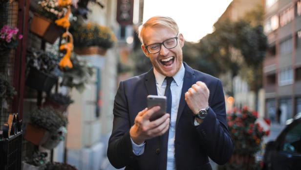 Mann im Anzug freut sich draußen über eine Nachricht auf seinem Smartphone.