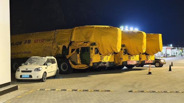 Mehrere Lkw mit gelben Planen und Zoomlion-Beschriftung stehen nachts auf einem Parkplatz.