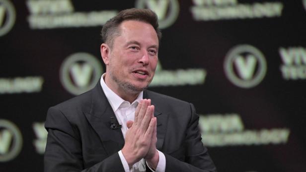 Elon Musk im Anzug hält die Hände zusammen.