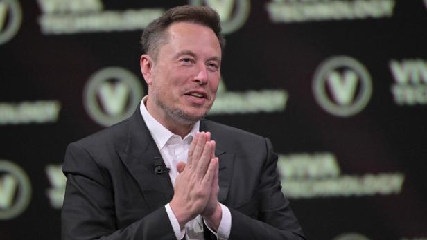 Elon Musk im Anzug hält die Hände zusammen.