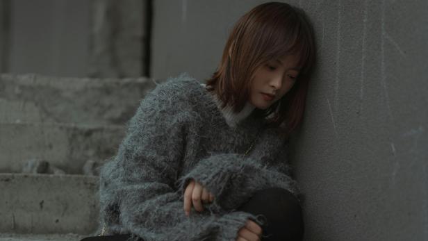 Junge Chinesin mit flauschigem Pullover sitzt alleine in einem Innenraum.