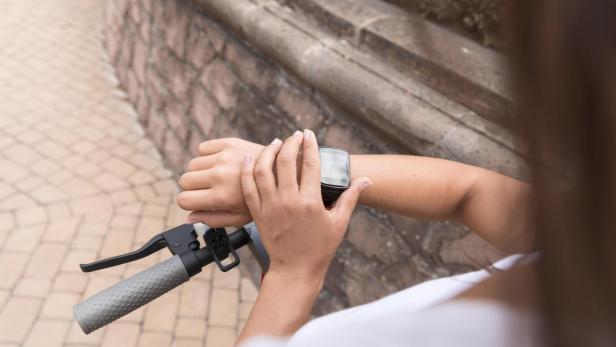 Eine Frau hält den Lenker ihres Fahrrads und drückt einen Knopf auf ihrer Smartwatch.