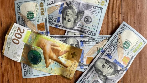 Mehrere 100-Dollar-Scheine und ein 200-Franken-Schein auf Holztisch.