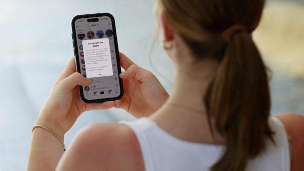 Eine Frau mit Zopf hält ein Smartphone und liest eine Benachrichtigung über aktualisierte Nutzungsbedingungen.